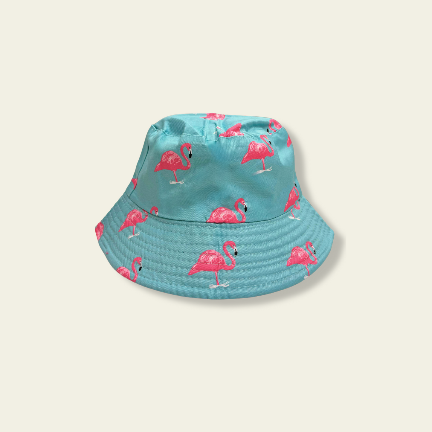 This reversible bucket hat is designed for children, offering protection from the sun with a functional and simple design. One side of the hat features a flamingo print in shades of blue and pink, while the reverse side is a pink solid color. Made from lightweight fabric, the hat is breathable and provides a comfortable fit for outdoor activities.