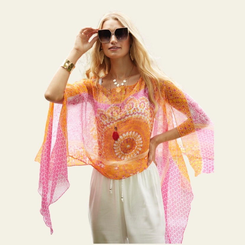 This lightweight chiffon poncho drapes beautifully, showcasing a vibrant blend of orange and pink. The model is posing, allowing the poncho to fall elegantly, highlighting its fluid and airy design—perfect for adding a touch of color to any outfit.