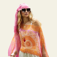 This lightweight chiffon poncho drapes beautifully, showcasing a vibrant blend of orange and pink. The model is posing, allowing the poncho to fall elegantly, highlighting its fluid and airy design—perfect for adding a touch of color to any outfit.