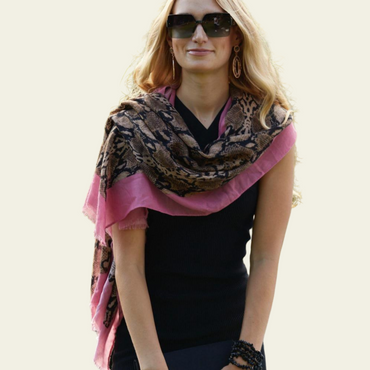 This animal print pashmina is elegantly draped over the shoulders of the model, showcasing its stylish design and soft, lightweight fabric. The pashmina features a bold animal print pattern, enhanced by a delicate pink border that adds a sophisticated touch.