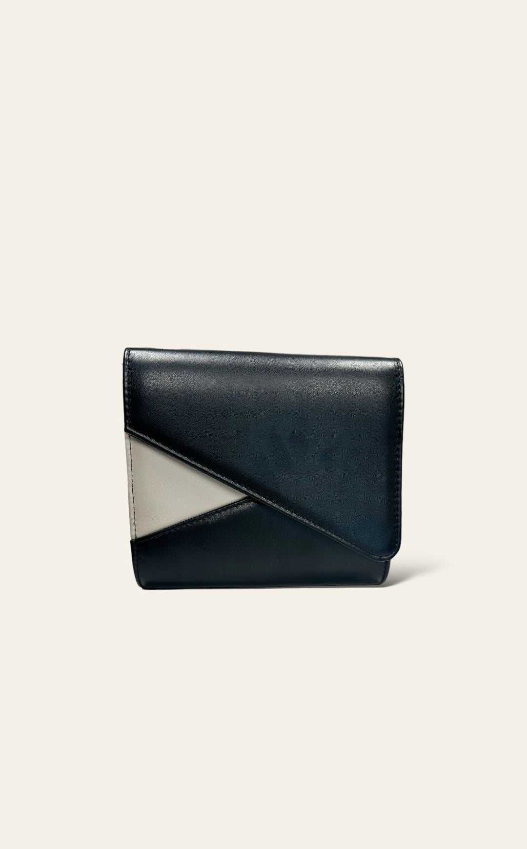 This black clutch features an asymmetrical design with a small ivory triangle accent. The simple and clean lines create a modern, minimalist look. Its compact size makes it practical for carrying essentials, and the subtle color contrast adds a refined touch.