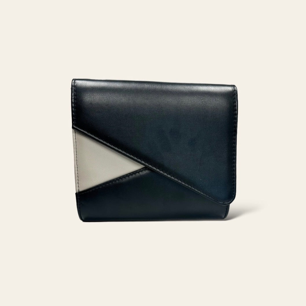 This black clutch features an asymmetrical design with a small ivory triangle accent. The simple and clean lines create a modern, minimalist look. Its compact size makes it practical for carrying essentials, and the subtle color contrast adds a refined touch.