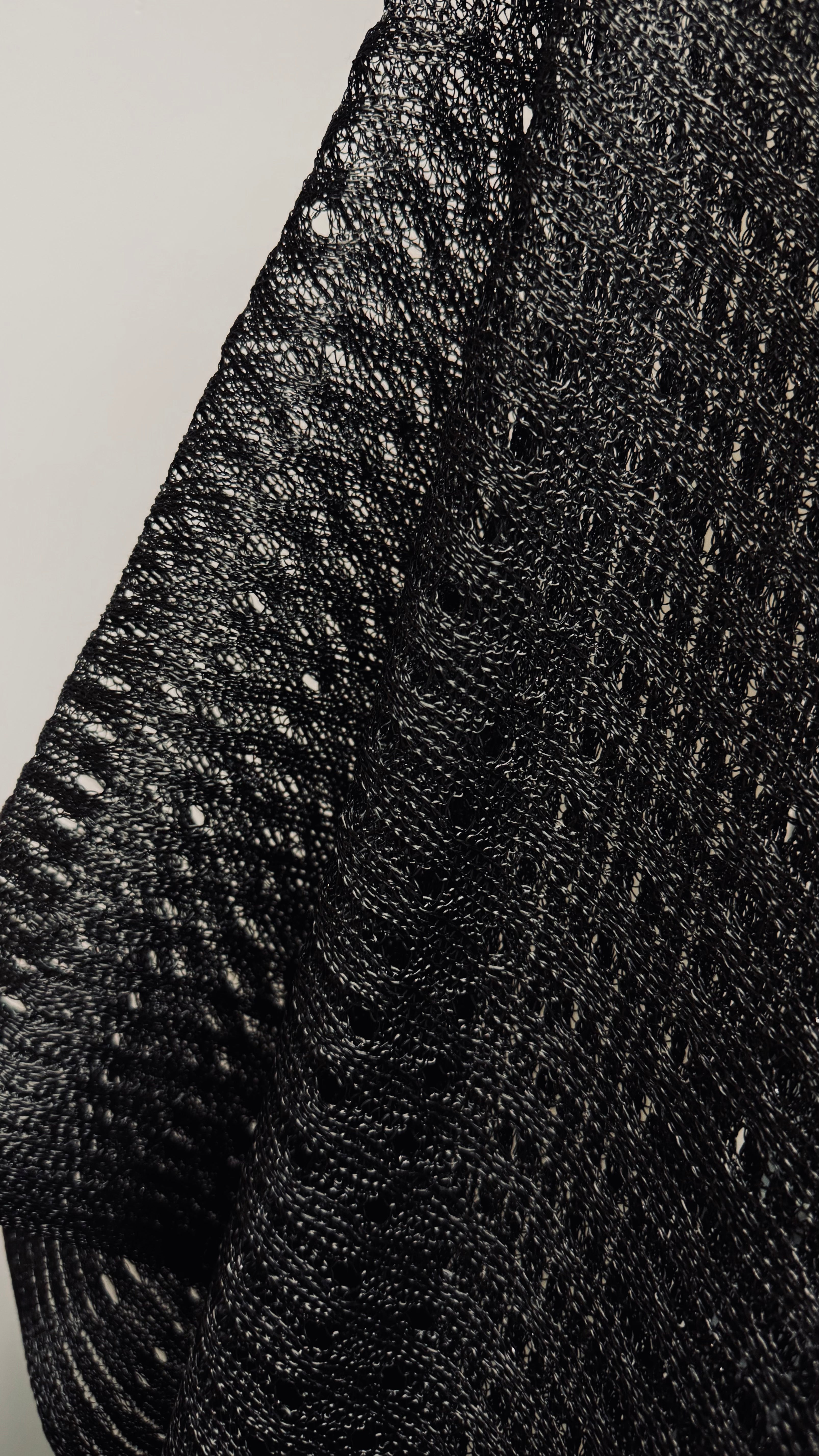  close-up of the black shawl, highlighting the intricate embroidery and small perforated spaces throughout the fabric. The detailed embroidery, combined with tiny holes or gaps, creates a delicate, lace-like effect. This design adds texture and visual depth to the shawl, enhancing its sophisticated appearance.