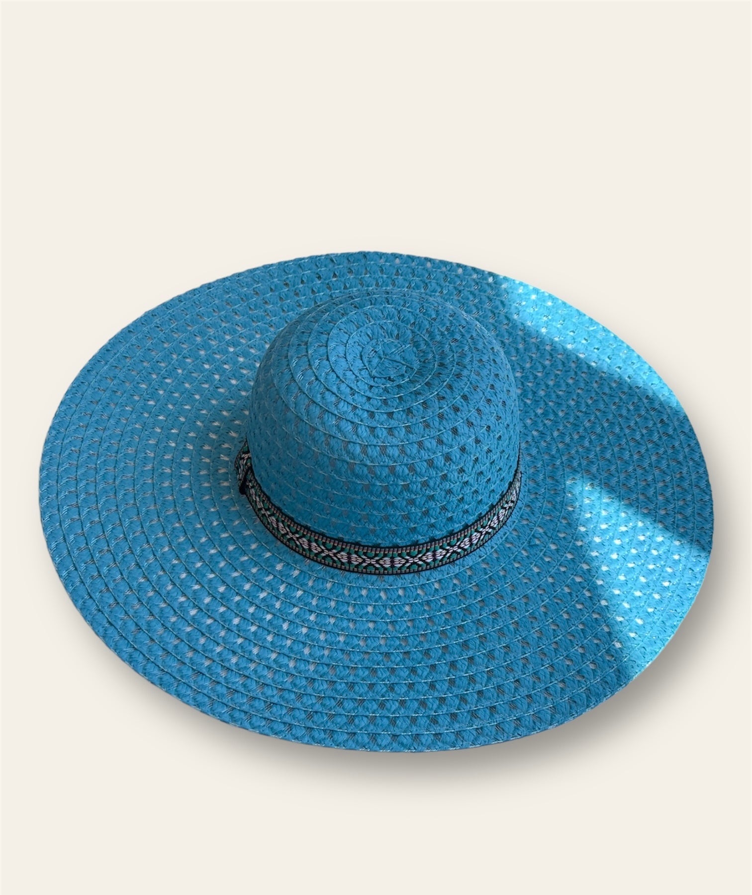 The hat is complemented by a sleek black band adorned with an abstract print adding a unique, artistic touch. The combination of the bold blue / turquoise with the contrasting black band creates a striking design that stands out while maintaining a stylish, modern aesthetic. Lightweight and comfortable, this hat offers sun protection and adds a pop of color to any outfit.