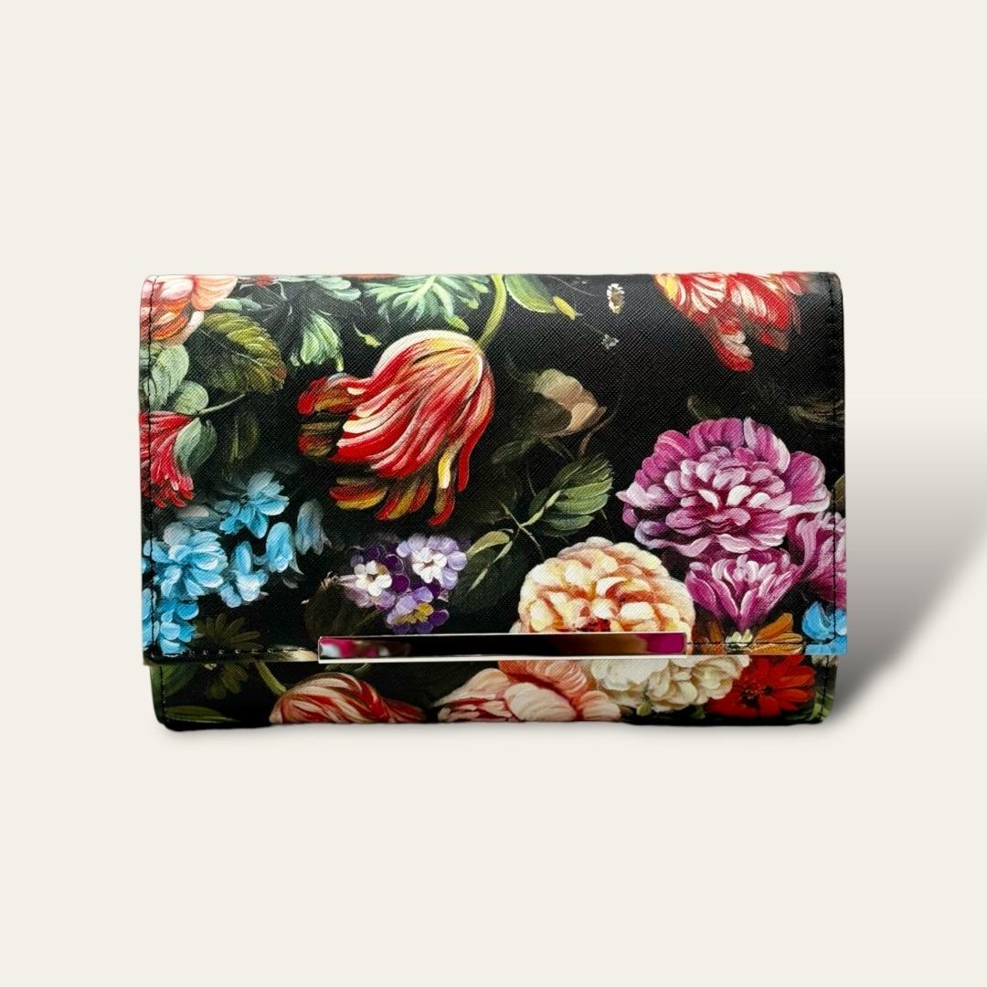 The Bijoux Terner Fashion Floral Print Clutch features a sleek black background that serves as a striking contrast to the vibrant, colorful floral print. The bold, intricate flowers in a mix of bright hues stand out against the light backdrop, creating a lively and eye-catching design. 