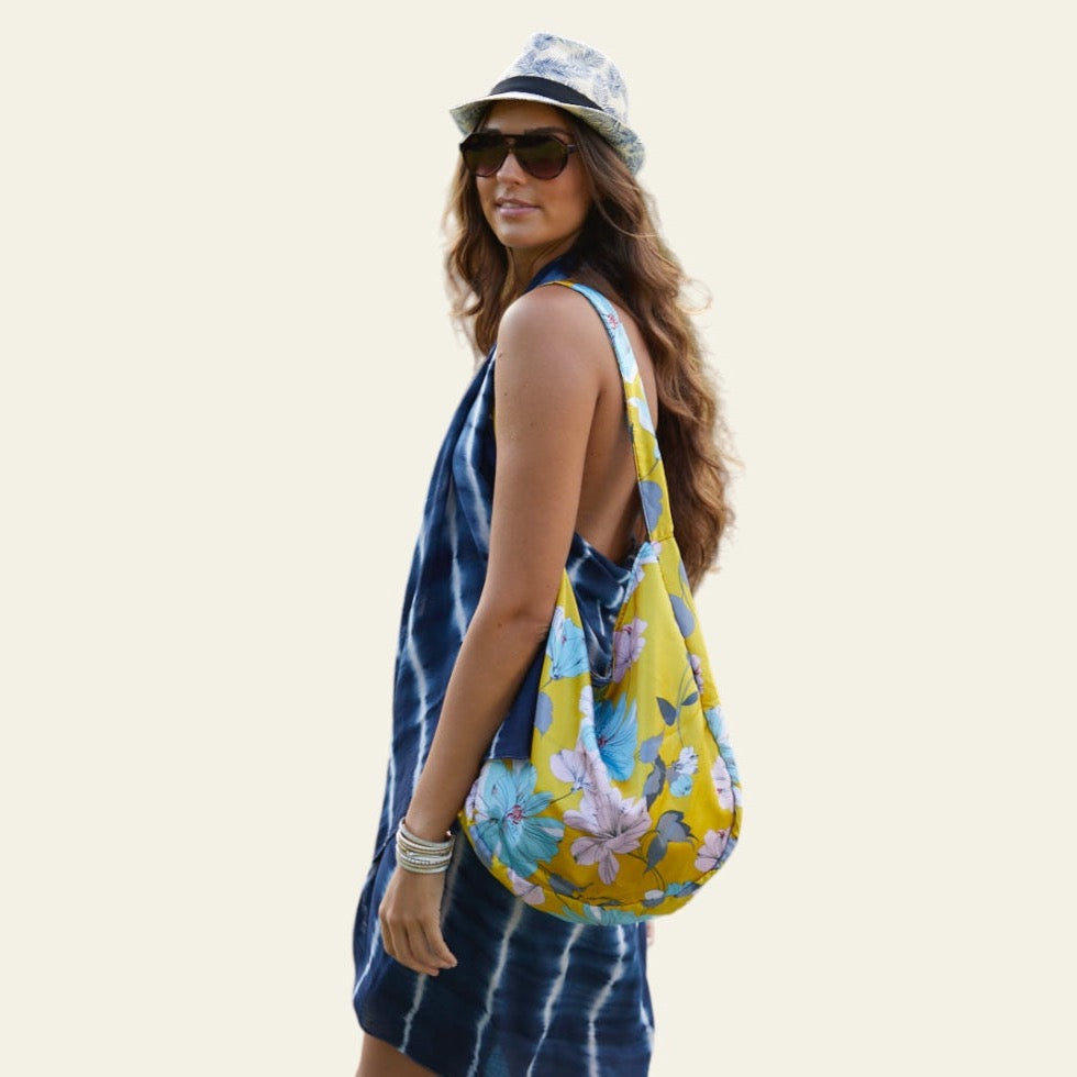 This Boho Bag features a striking floral print with vibrant, colorful flowers that beautifully contrast against the yellow background of the fabric. Crafted from a silky material, the bag offers a smooth feel while maintaining durability and flexibility. Its foldable design adds a practical element, allowing for easy storage and portability. 